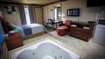Habitación de hotel con cama, escritorio, silla, sillón de cuero rojo, televisor, refrigerador y bañera.