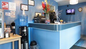 Un área de recepción con un mostrador azul, una máquina de café, un dispensador de agua y un cubo de basura.