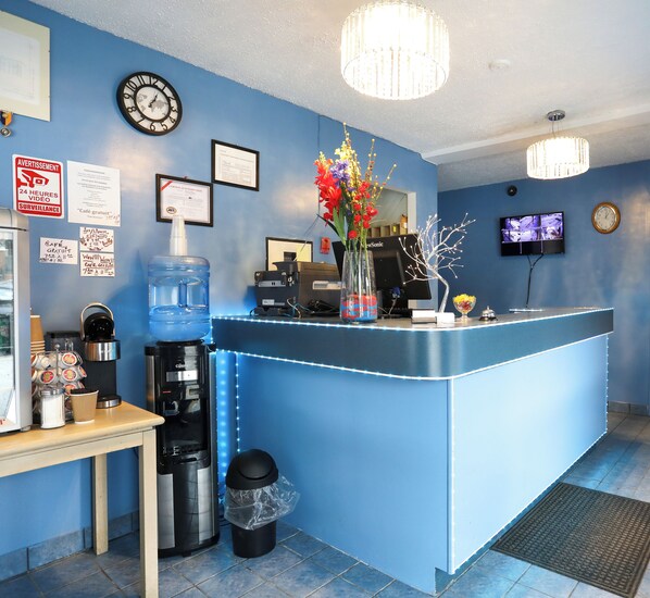 A reception area with a blue counter, a coffee machine, a water dispenser, and a trash can. - Motel LeClassique (Saint-Charles-Borromée)