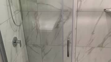 Cabina de ducha con paredes de vidrio, una alcachofa de ducha manual y un grifo manual.