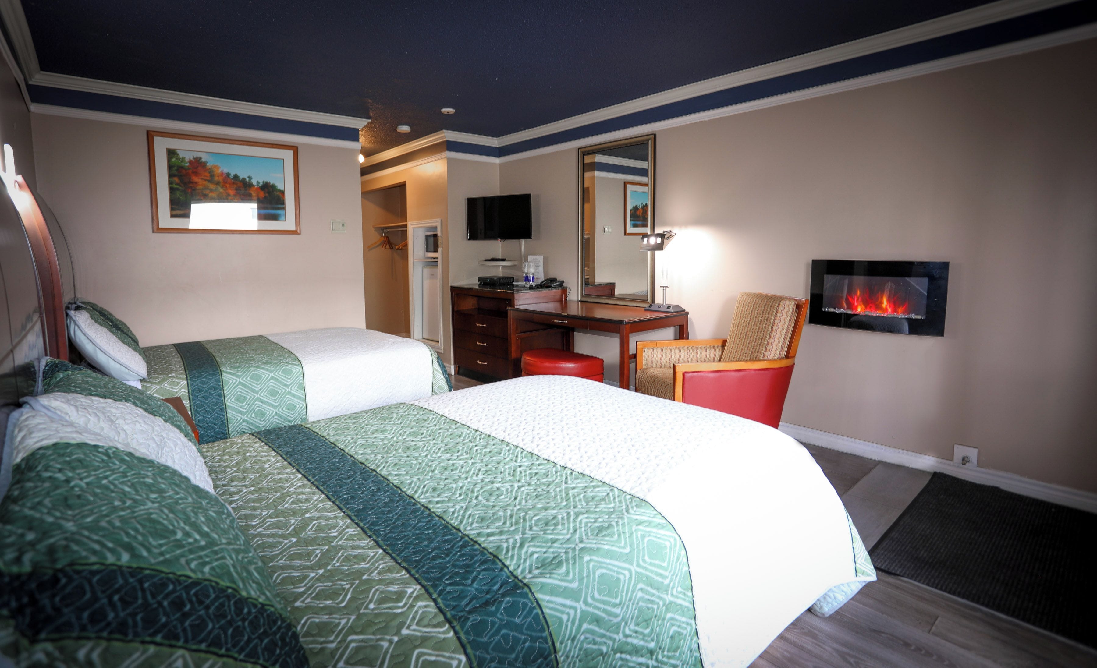 A hotel room with two beds, a desk, a chair, a television, and a fireplace.