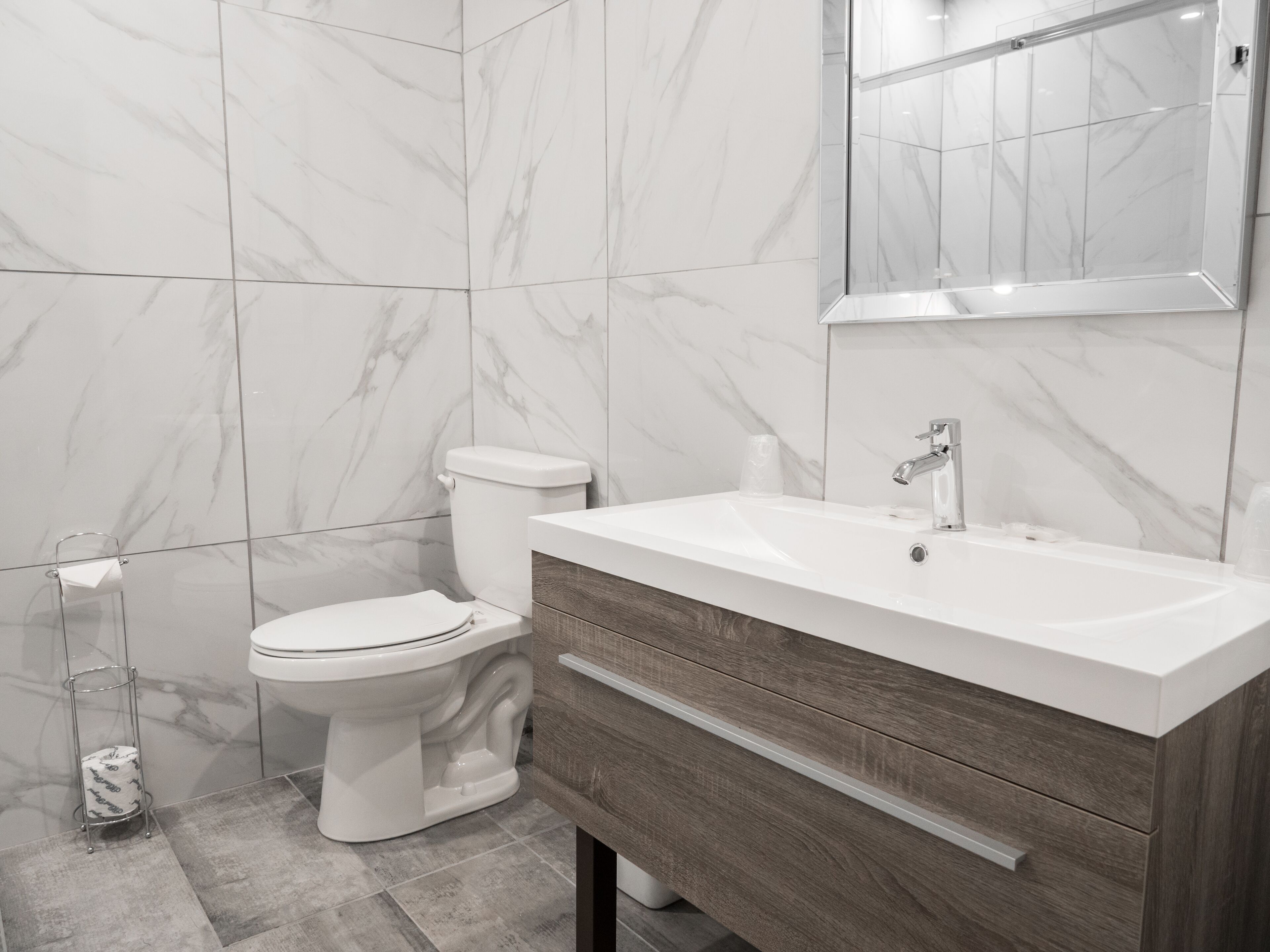 A modern bathroom with a white toilet, a wooden vanity with a sink, and a mirror above the sink.