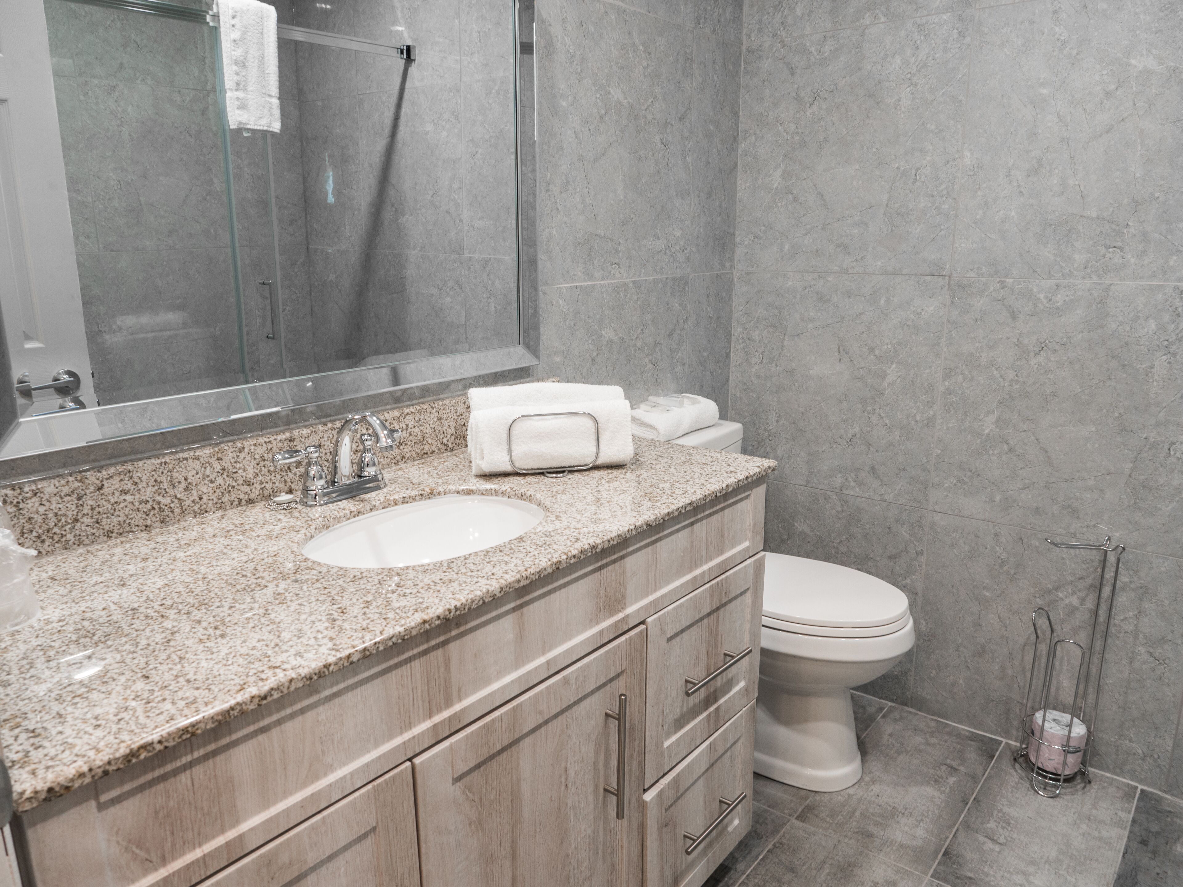 A modern bathroom with a granite countertop, a double sink, a toilet, and a shower area.