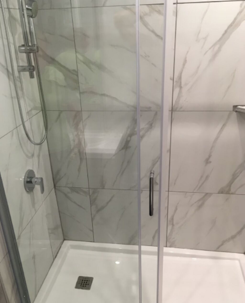 Una ducha con puerta de vidrio, cabezal de ducha de mano y grifo empotrado en la pared.