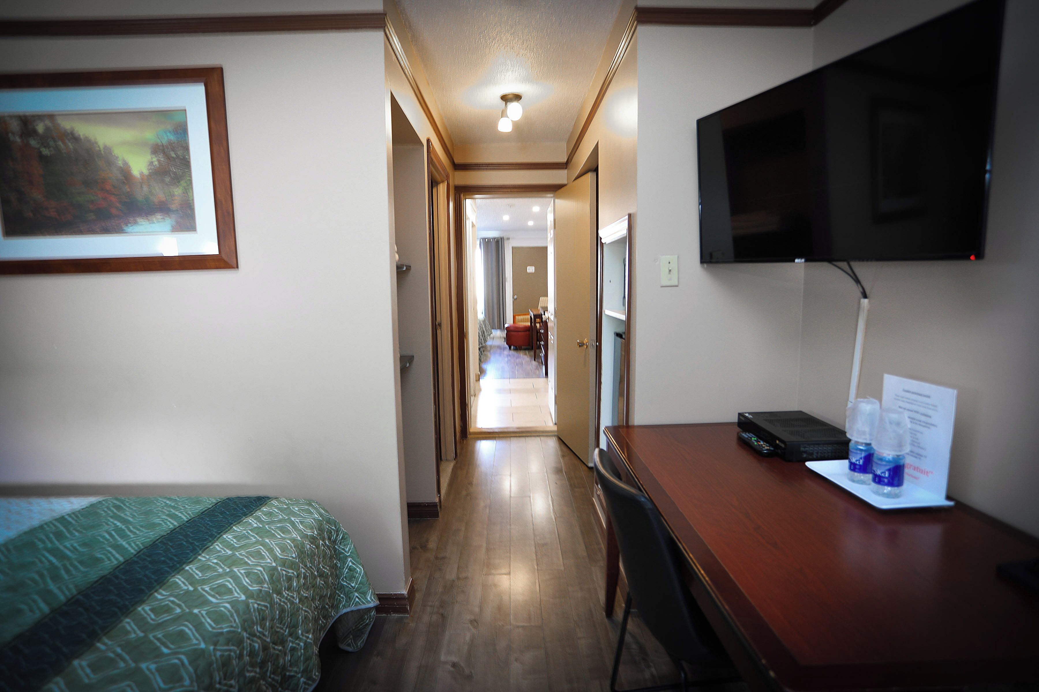 Una habitación de hotel con cama, escritorio, televisor y un pasillo que conduce a otra habitación.