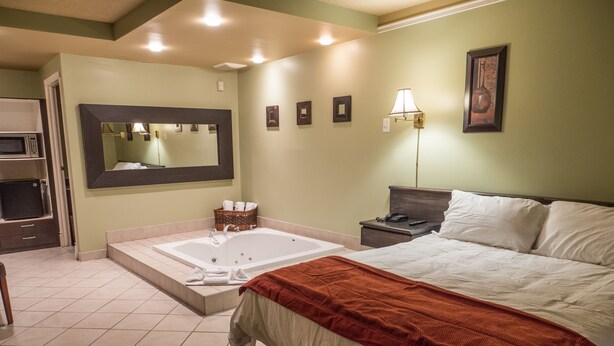 Habitación de hotel con una cama grande, baño independiente con bañera, microondas y una pequeña mesa con lámpara.