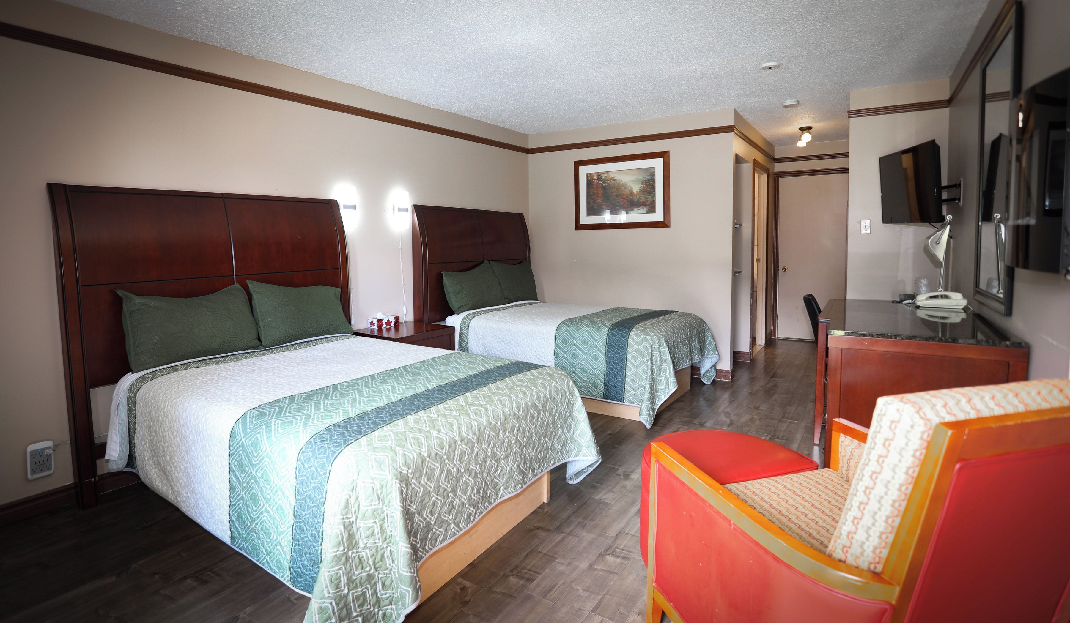 A hotel room with two beds, a desk, a chair, and a television.