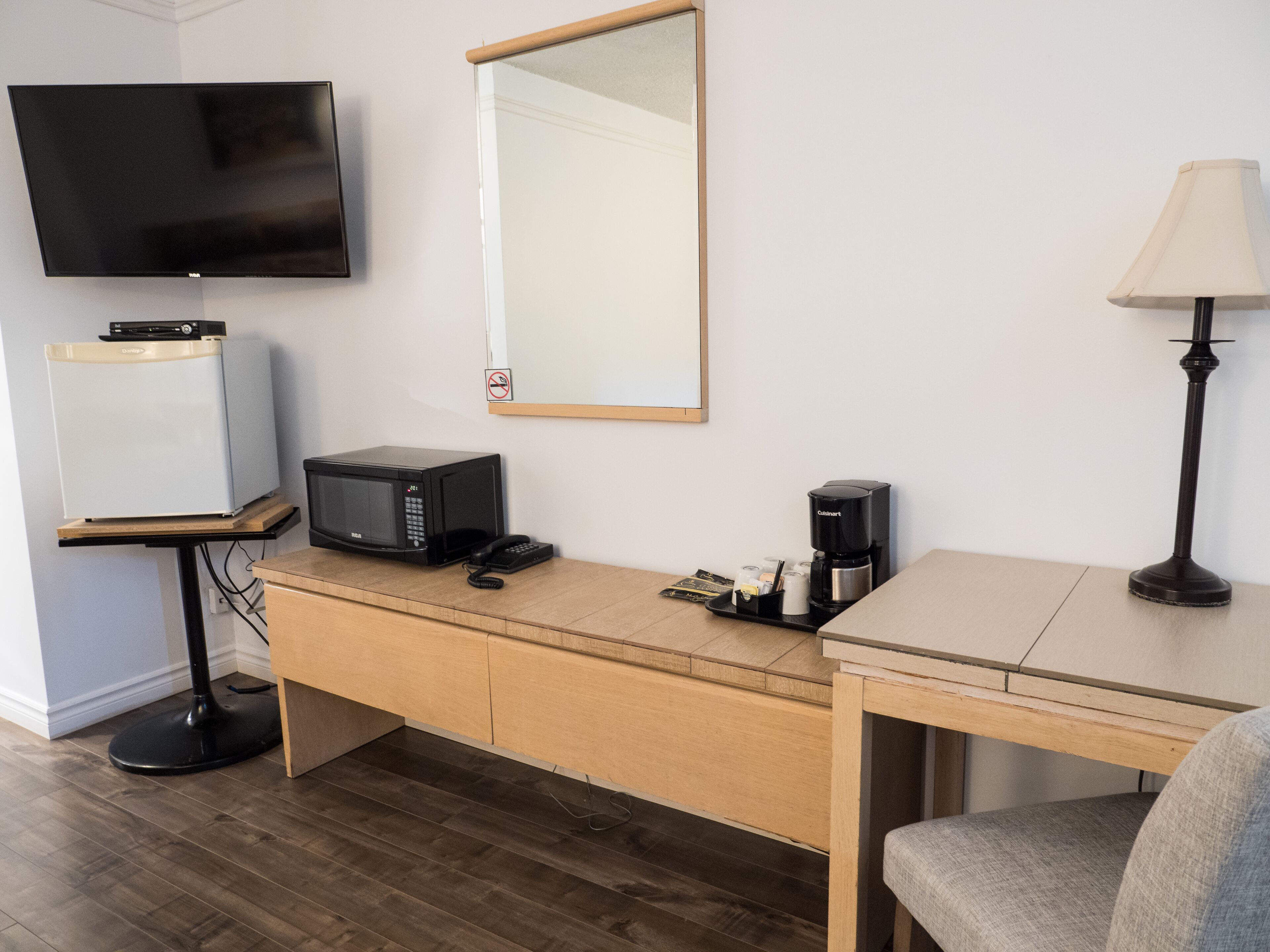 A hotel room with a flat-screen TV, a microwave, a coffee maker, a desk, and a chair.
