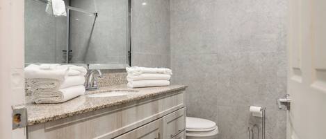Un baño moderno con encimera de granito, lavamanos, inodoro y cabina de ducha con mampara de vidrio.