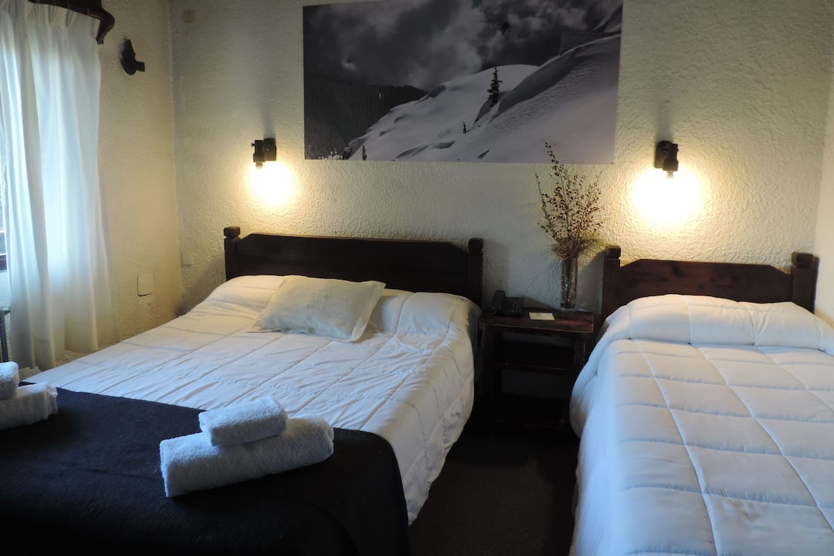 Ein Hotelzimmer mit zwei Betten, einem Gemälde einer verschneiten Landschaft und Wandleuchten.