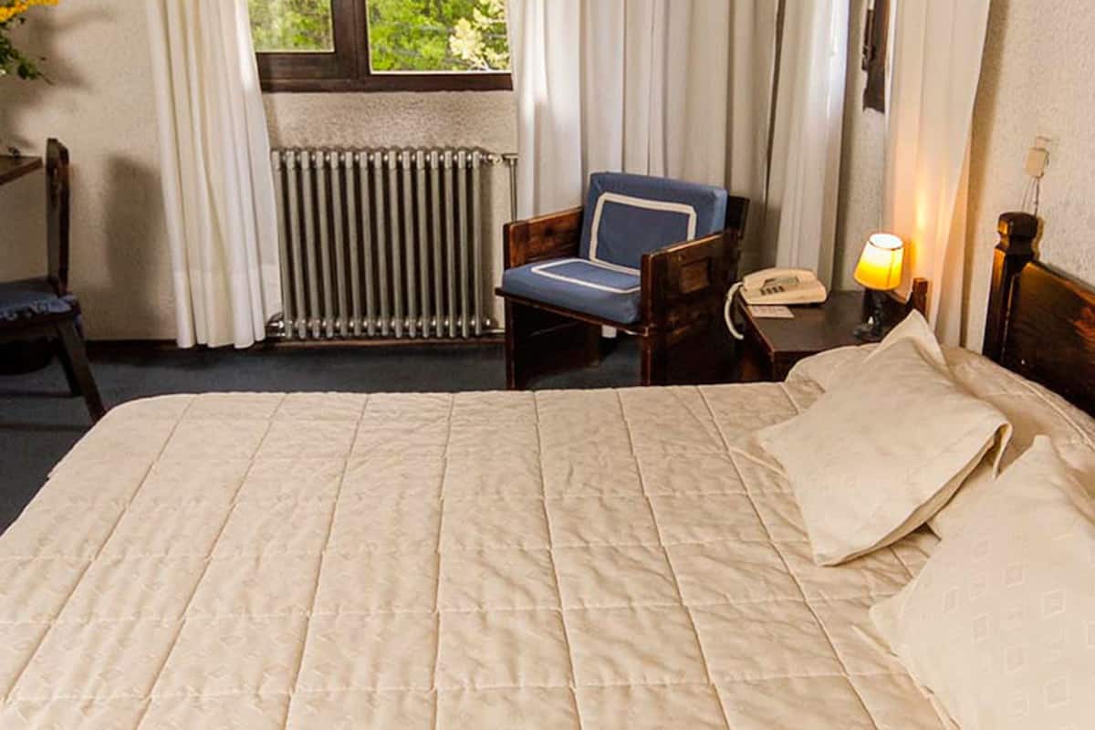 Ein Hotelzimmer mit einem großen Bett, einem Sessel, einem Nachttisch mit Lampe und einer Heizung.