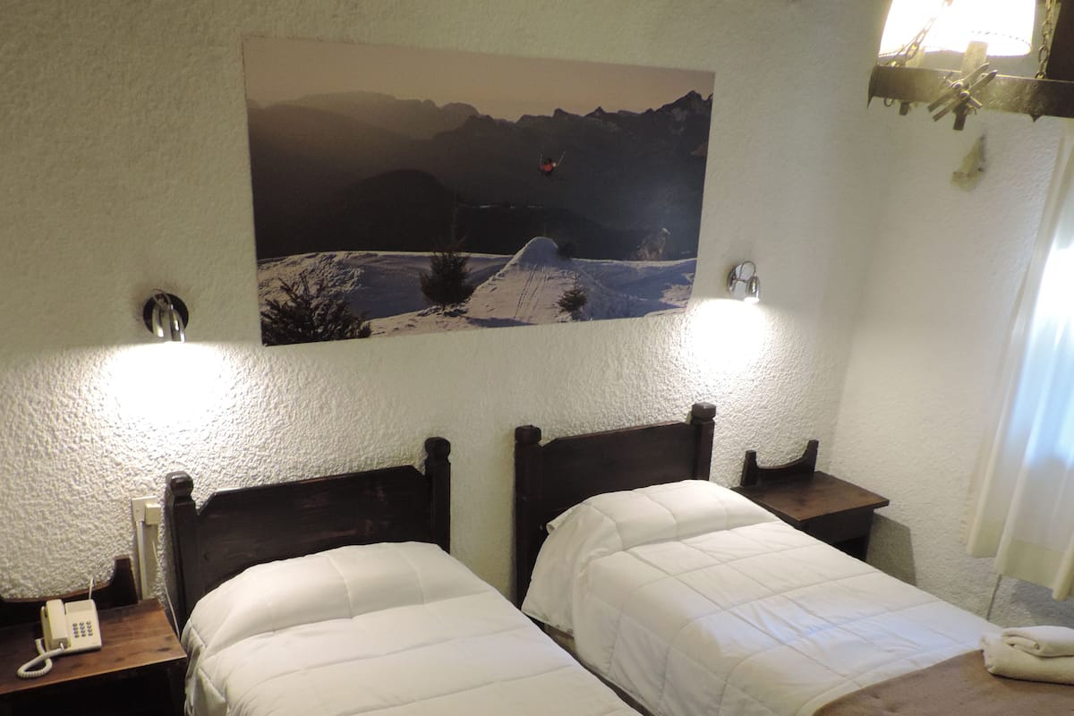 Ein Hotelzimmer mit zwei Betten, einem Berglandschaftsbild, einem Telefon auf dem Nachttisch und einer Lampe.