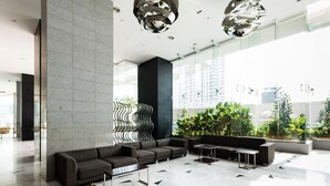Eine moderne Lobby mit Ecksofa, Couchtisch und einer Glaswand mit Blick auf Grünflächen und Gebäude.
