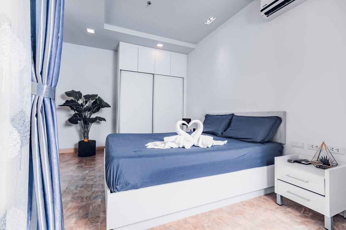 A modern bedroom with a bed, a nightstand, a potted plant, and a wardrobe.