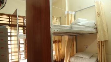 A bunk bed room with a wooden partition, a fan, and a window with curtains.