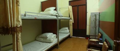 A dormitory room with bunk beds, a wooden floor, a chair, and a wardrobe.