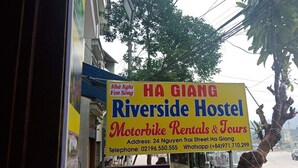 A sign for Ha Giang Riverside Hostel advertising motorbike rentals and tours.