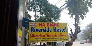A sign for Ha Giang Riverside Hostel advertising motorbike rentals and tours.