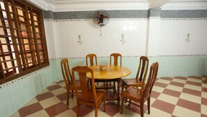 A dining area with a checkered floor, wooden chairs, a round table, and a fan on the wall.