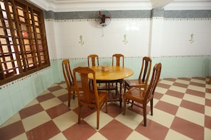 A dining area with a checkered floor, wooden chairs, a round table, and a fan on the wall.