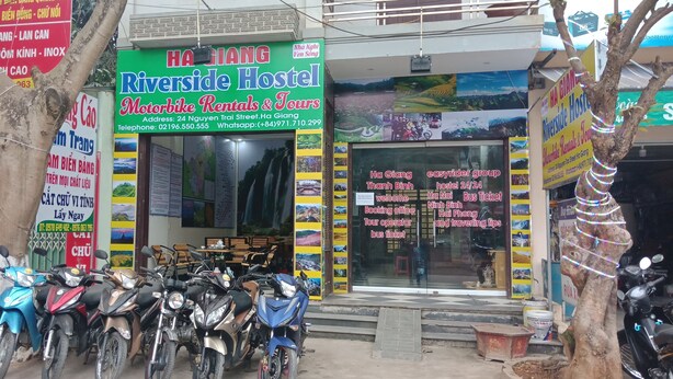 A Riverside Hostel with a signboard advertising motorbike rentals and tours.