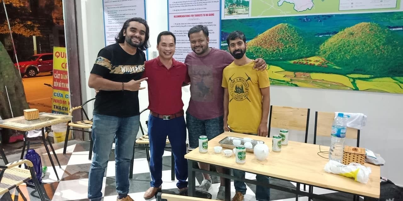 A group of four people standing in a room with a table displaying cans and a map on the wall.