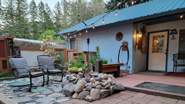 Un bâtiment de style rustique, à la façade bleue, doté d’une terrasse en pierre et d’un espace extérieur aménagé avec deux chaises.
