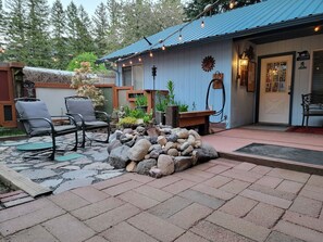 Un bâtiment de style rustique, à la façade bleue, doté d’une terrasse en pierre et d’un espace extérieur aménagé avec deux chaises.
