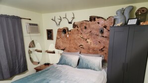 Une chambre à coucher avec une tête de lit en bois rustique, un lit recouvert d’une couvre-lit à motifs bleus et blancs, une armoire en bois et un miroir fixé au mur.
