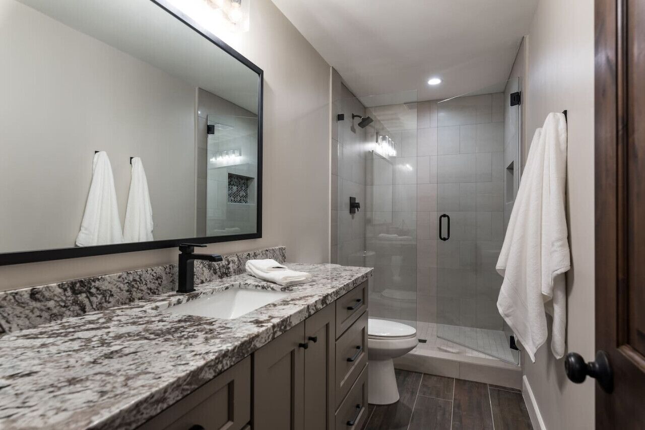 Een moderne badkamer met een marmeren wastafel, een toilet en een douche met glazen wanden.