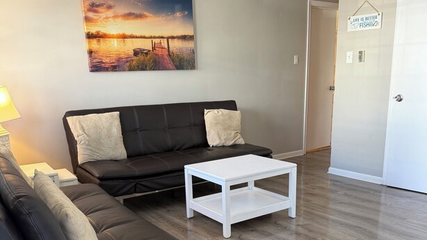 A modern living room with a black leather sofa, a white coffee table, and a painting of a sunset over water. - Close to beach! Spacious -Condo B (Ocean City)