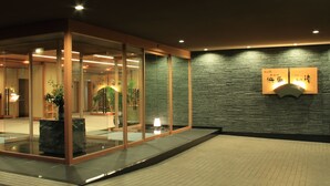 A modern hotel lobby with glass doors, a reception desk, and a wall-mounted sign. - Yumotokan New Hamajima (Shima)