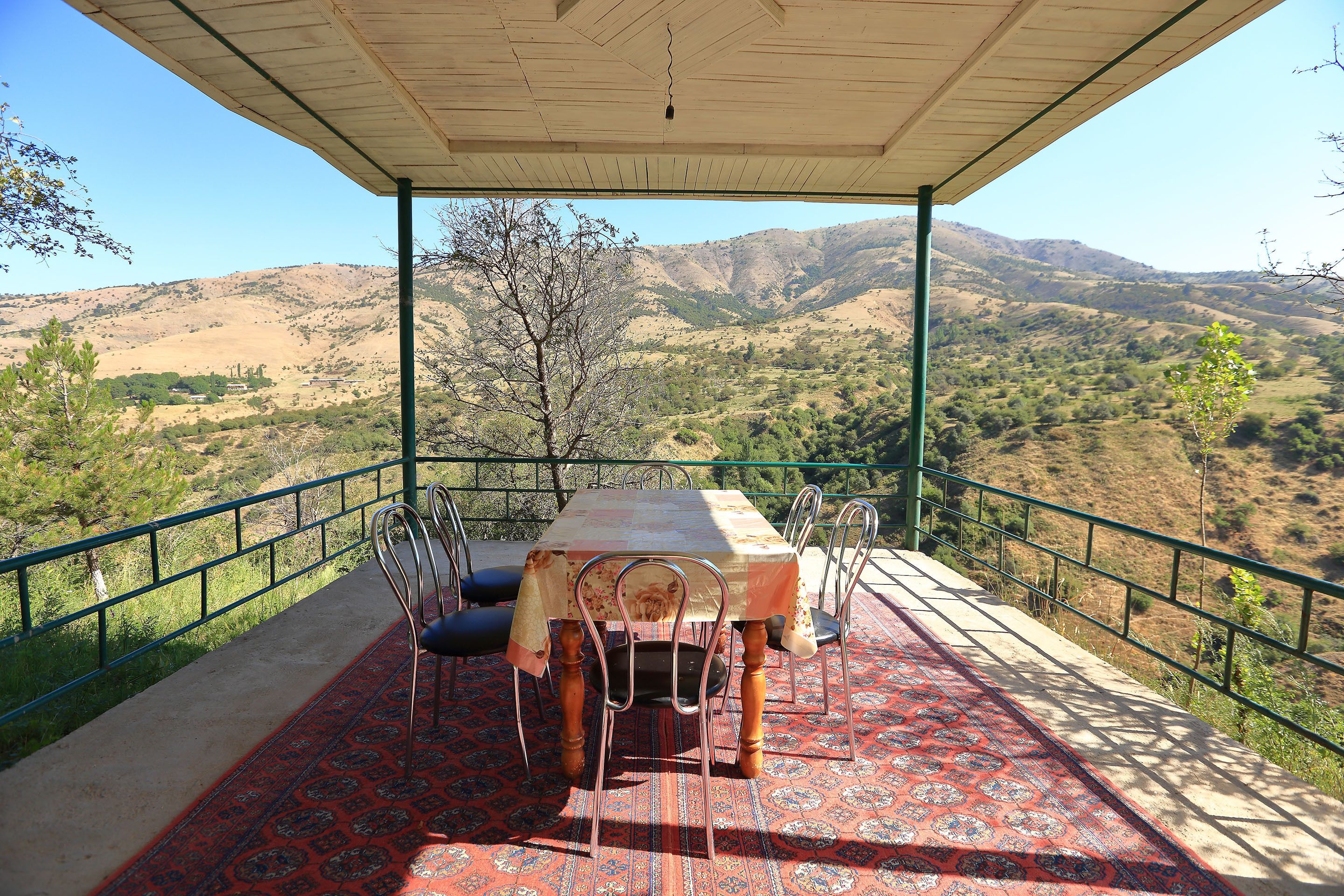 An outdoor terrace with a table and chairs, overlooking a mountainous landscape.