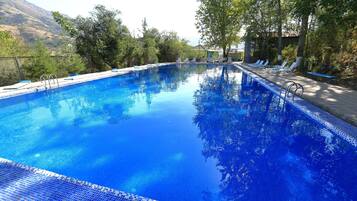 Relax by the serene pool surrounded by lush greenery and rolling hills, with lounge chairs for ultimate comfort.