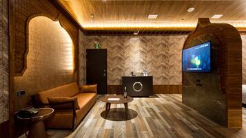 A modern lounge area with a herringbone-patterned wall, a comfortable sofa, a coffee table, a television, and a decorative cabinet.
