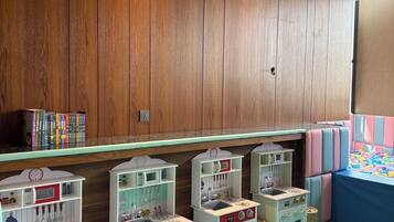 A children's play area with wooden panel walls, a green floor, and multiple play kitchens.