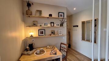 Un coin repas accueillant avec une table en bois, des chaises et un plateau contenant des tasses et une bougie. Des étagères au-dessus de la table sont ornées de photos encadrées et d’objets décoratifs.
