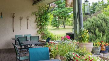 An outdoor patio with green chairs and tables, surrounded by potted plants and flowers.
