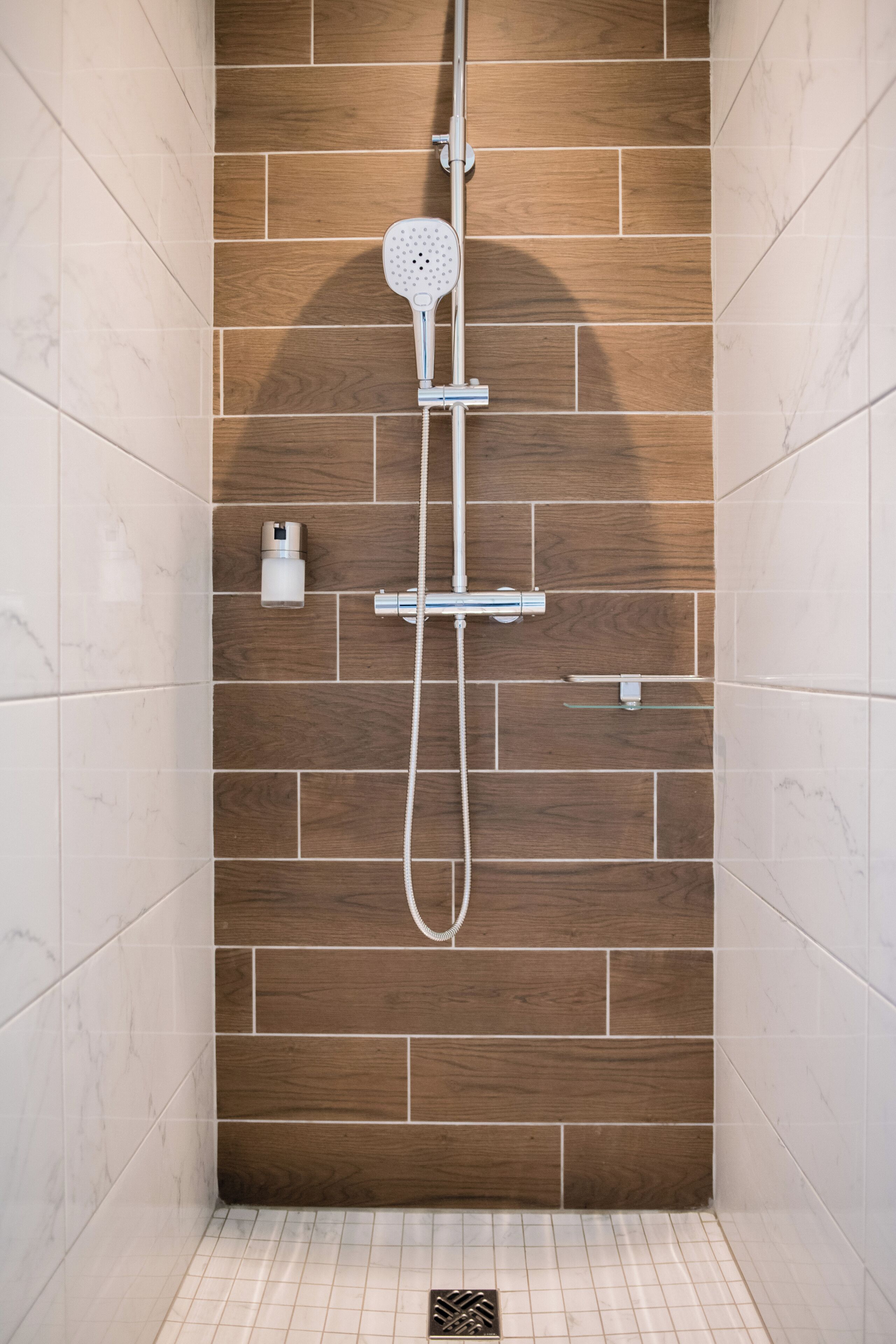 A shower with a wooden wall, a handheld showerhead, and a wall-mounted faucet.