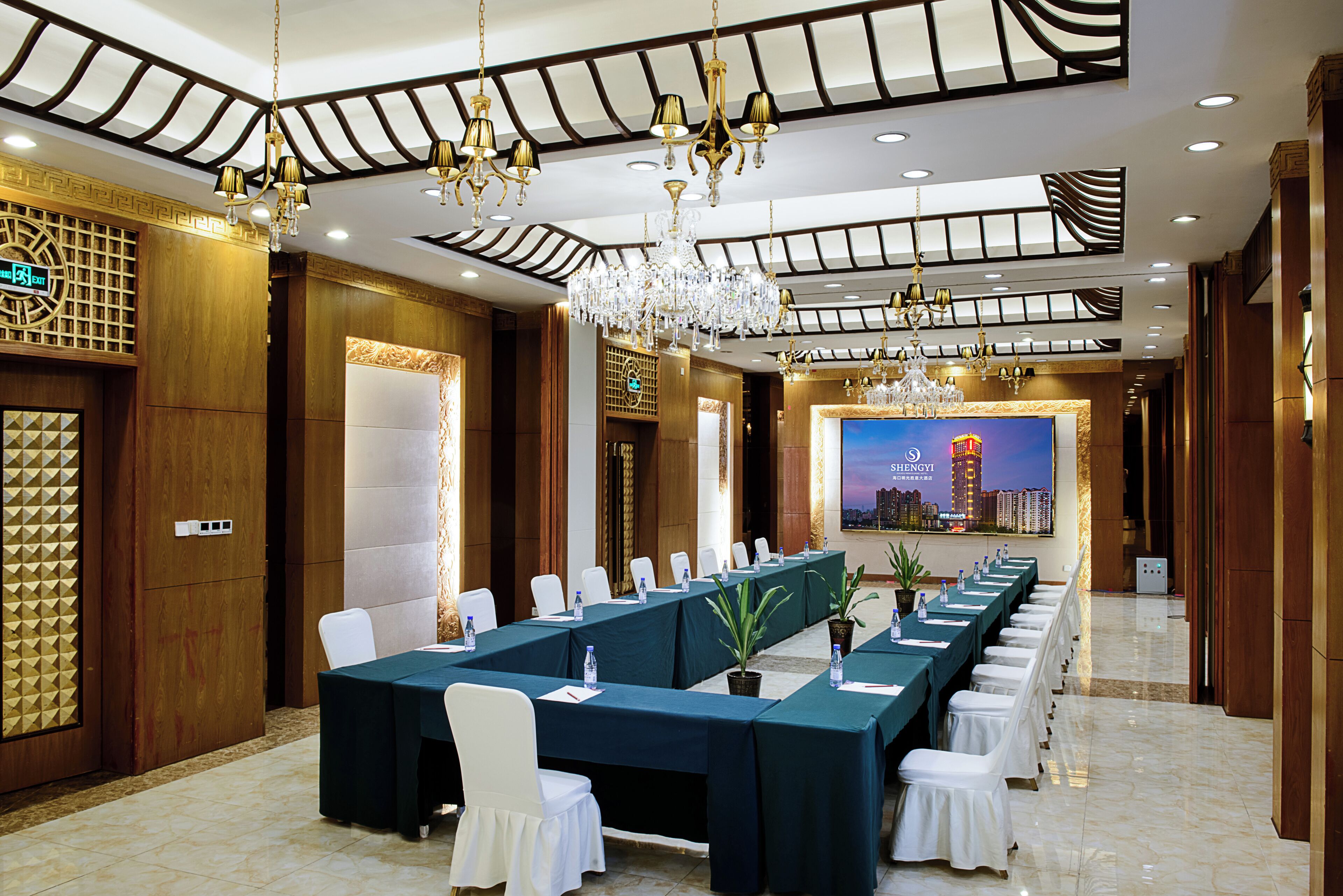 Un salón de conferencias con una larga mesa, sillas blancas y vistas a la ciudad.