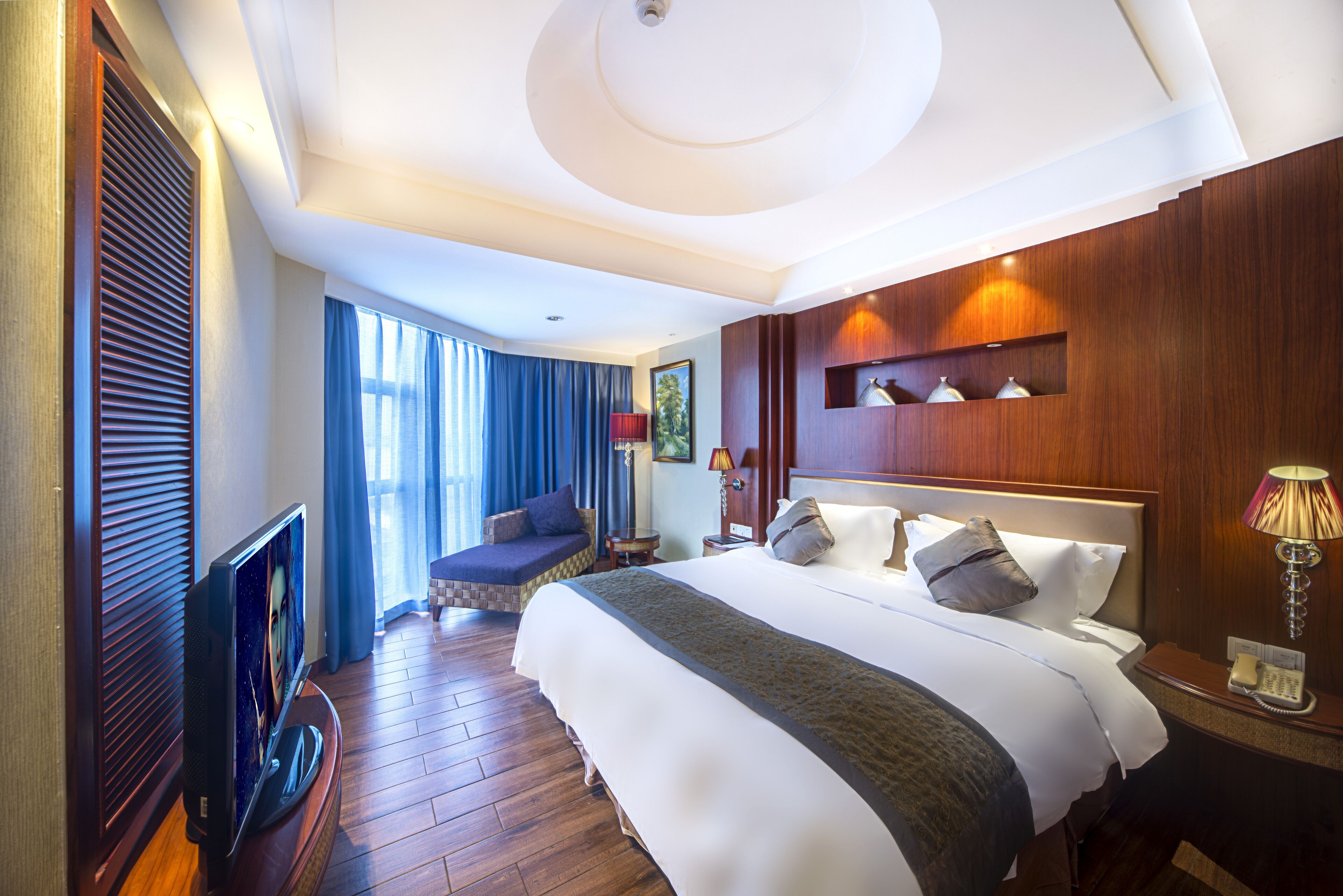 Een hotelkamer met een groot bed, een televisie, een zithoek en een houten wand met planken.