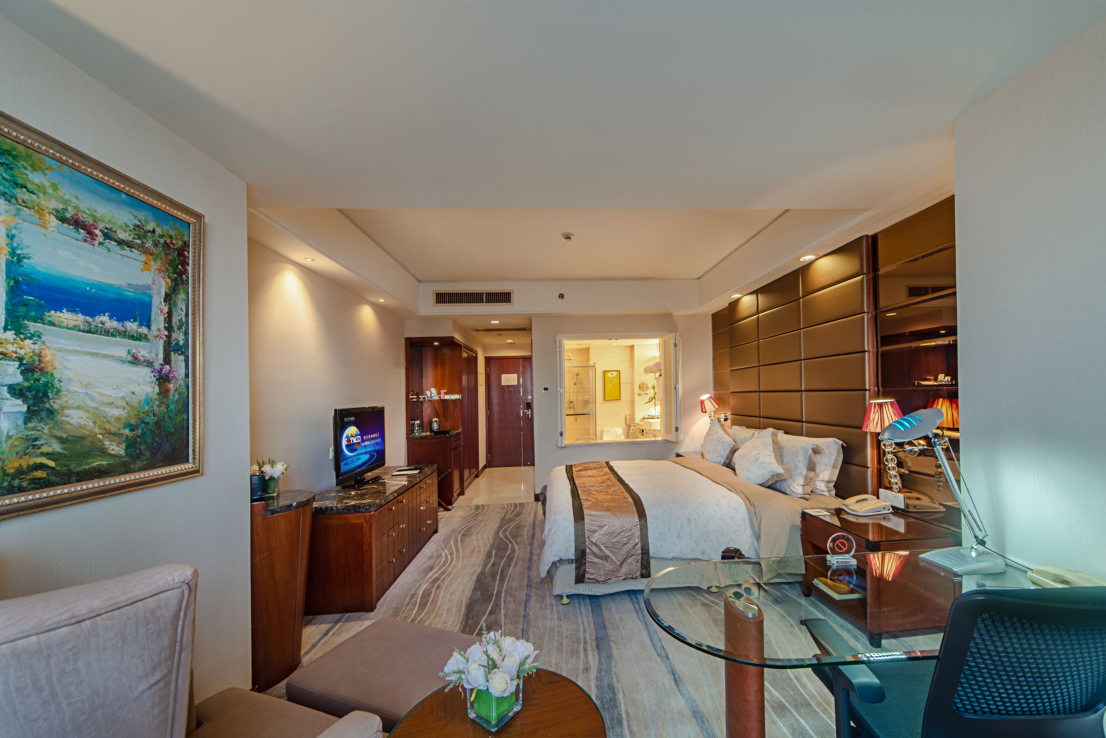 Una habitación de hotel con cama, escritorio, televisión, baño y un cuadro grande en la pared.