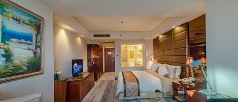 Una habitación de hotel con cama, escritorio, televisión, baño y un cuadro grande en la pared.