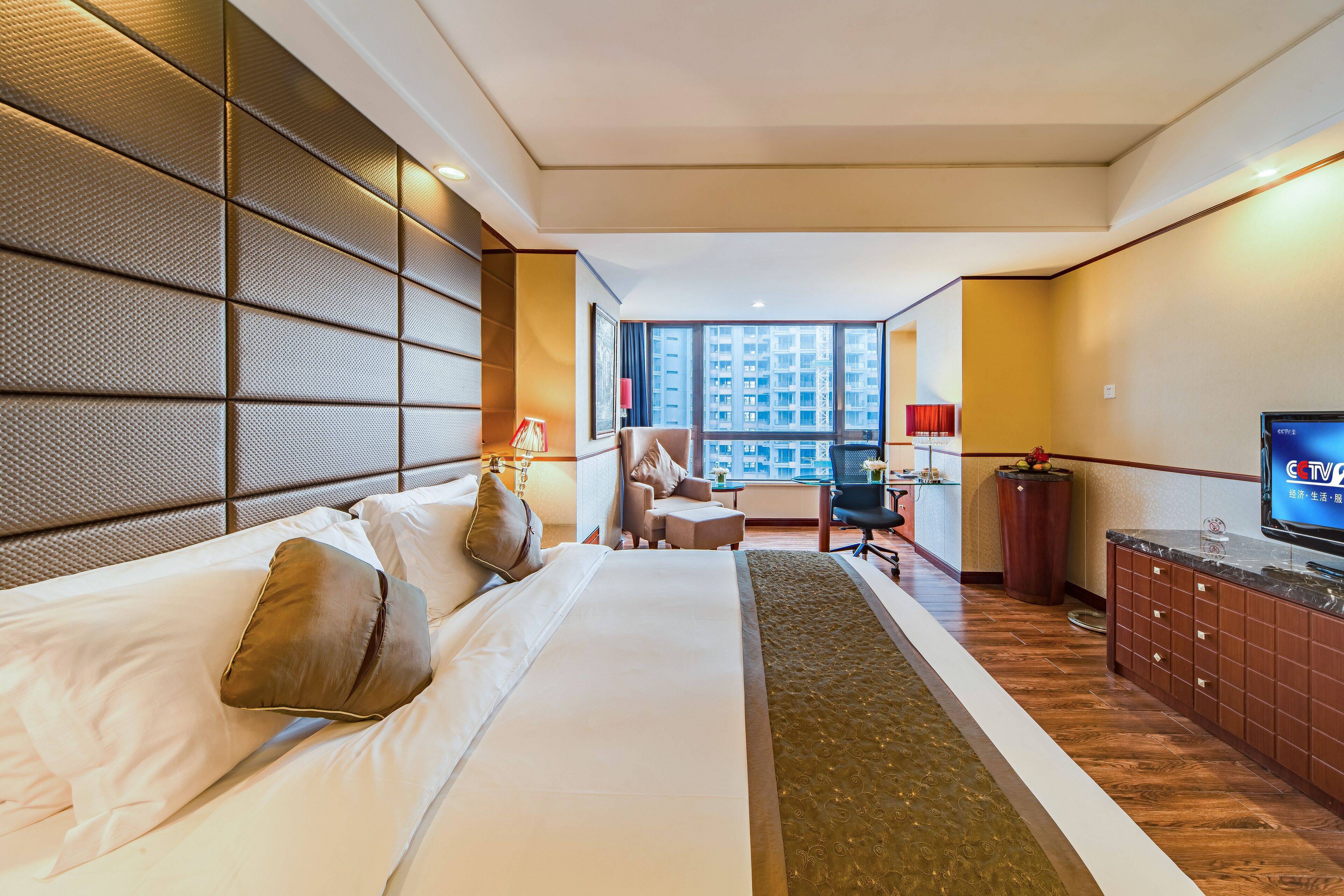 A hotel room with a large bed, a desk, a chair, and a TV.