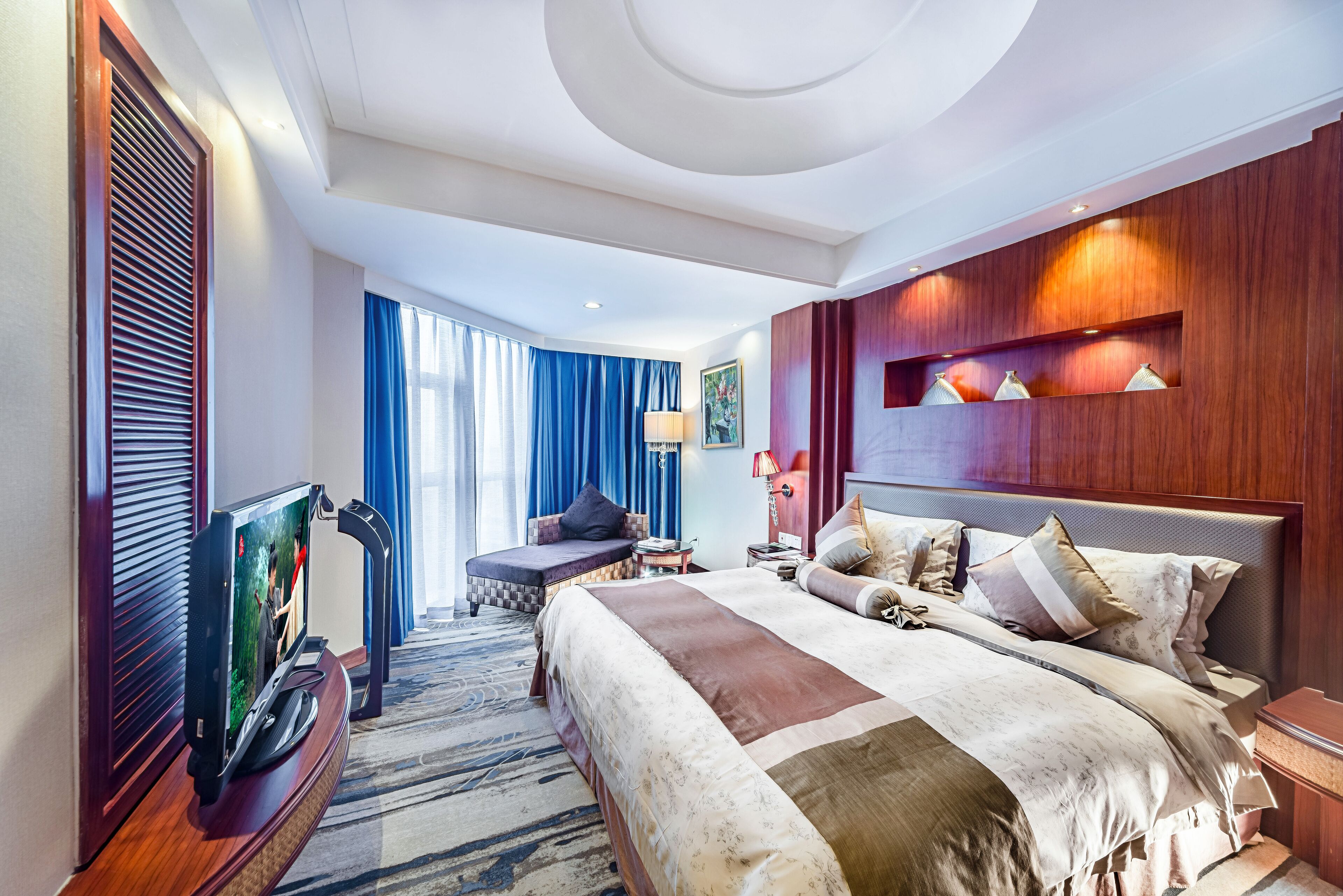 Ein modernes Hotelzimmer mit einem großen Bett, einem Fernseher, einer Sitzecke und Blick ins Freie.