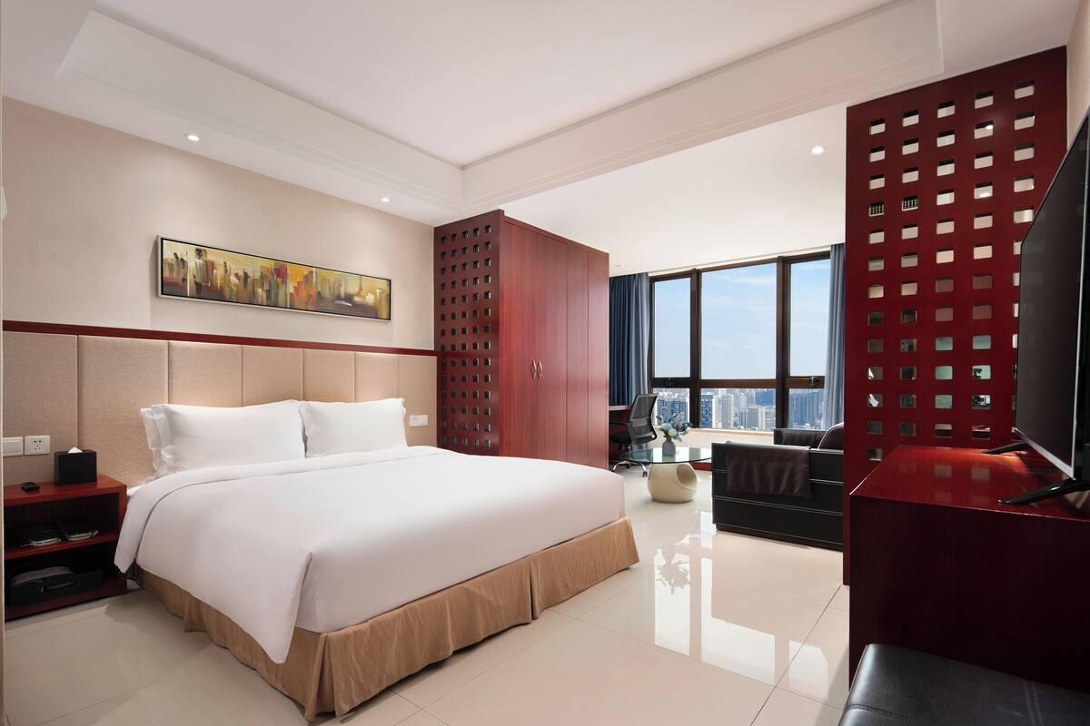 A modern hotel room with a large bed, a desk, a TV, and a city view.