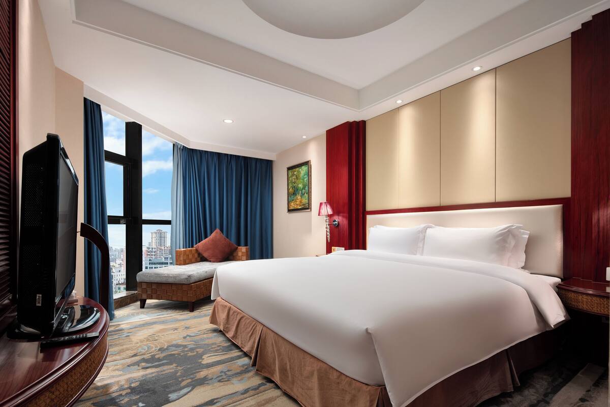 A hotel room with a large bed, a television, a sofa, and a view of the city.