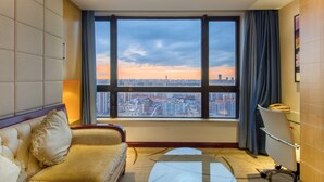 A hotel room with a large window offering a city view, a sofa, a desk, and a chair. - Haikou Mingguang Shengyi Hotel (Haikou)