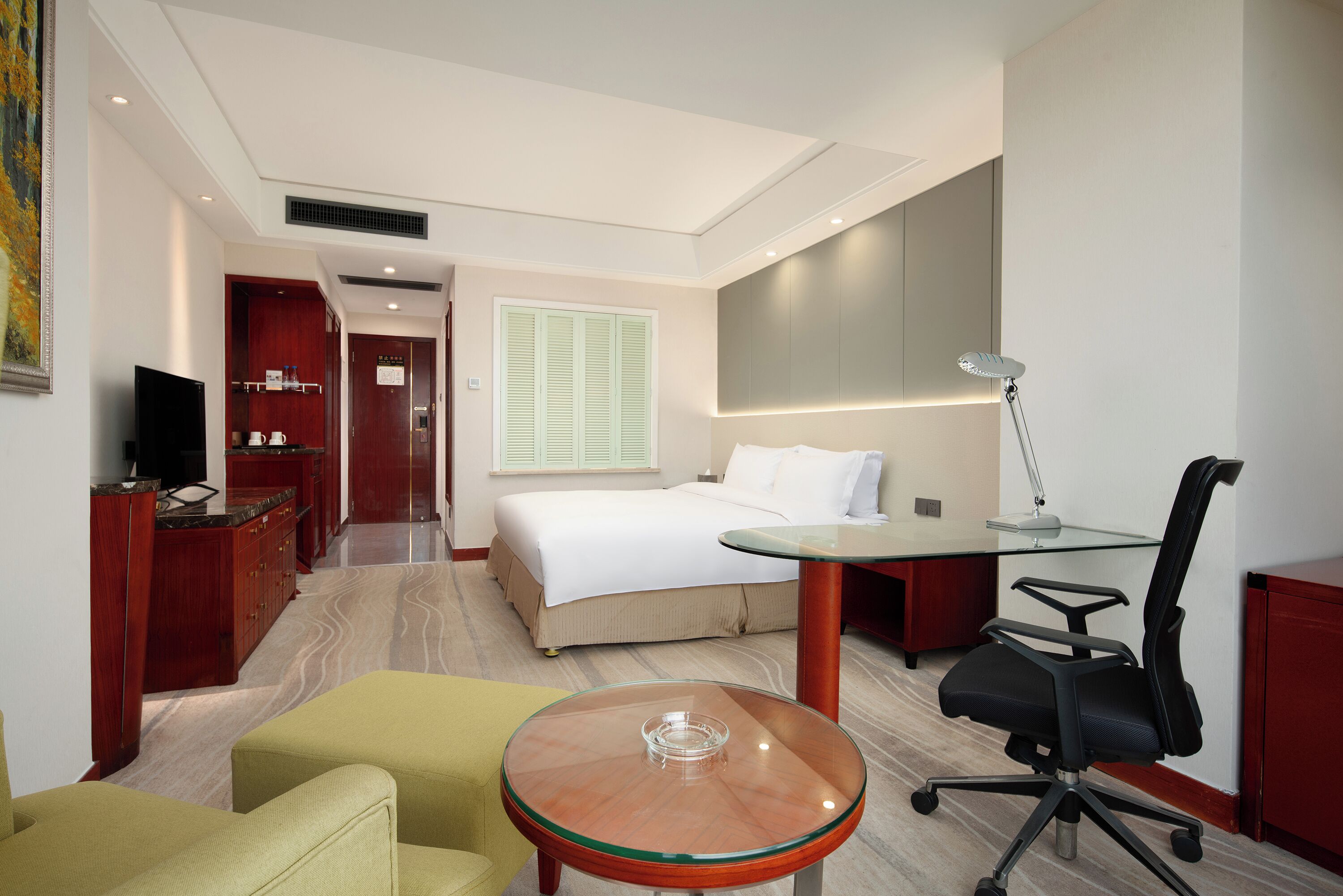 A hotel room with a bed, desk, chair, and a TV.