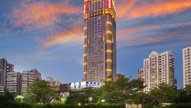 A high-rise building with multiple floors, surrounded by other buildings and greenery. - Haikou Mingguang Shengyi Hotel (Haikou)